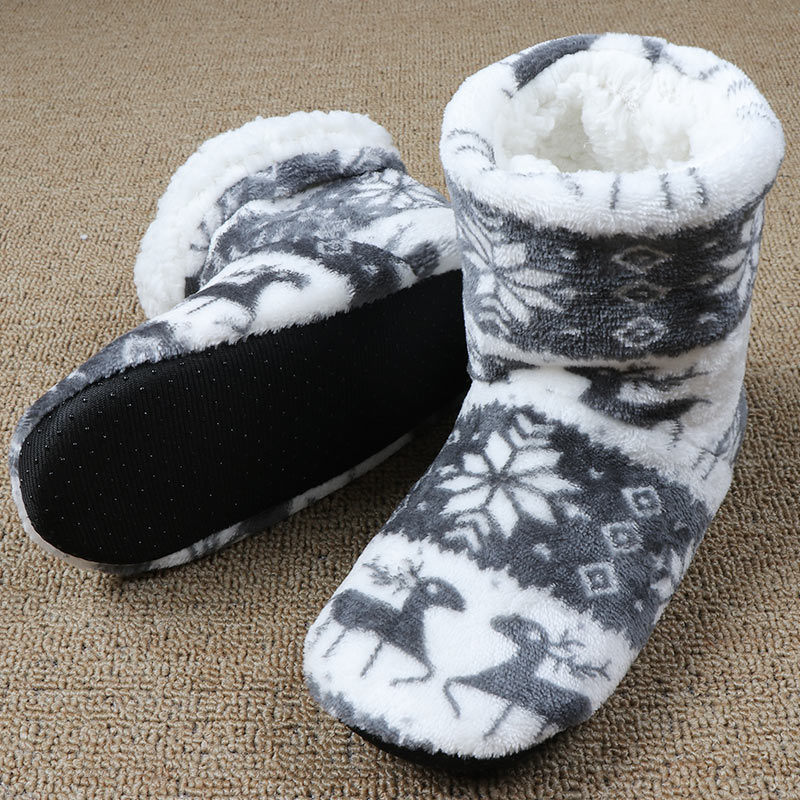 Cozy fleece slippers with a black sole, featuring a gray and white snowflake and reindeer pattern, placed on a textured beige carpet.