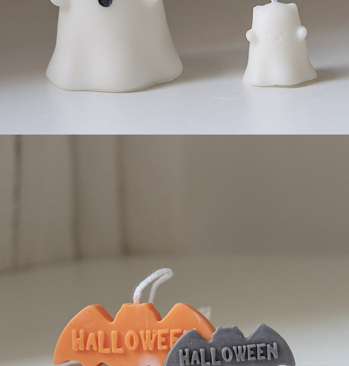 Two ghost-shaped candles, one large and one small, are on a white surface. Below them, two bat-shaped candles in orange and gray with "Halloween" text are visible.