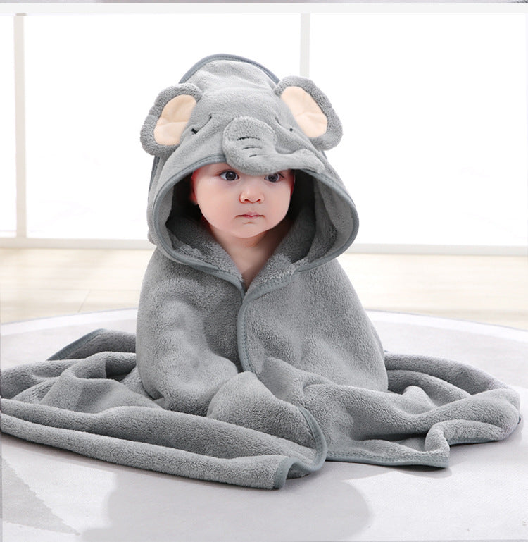 A baby sits wrapped in a soft gray blanket with an elephant hood, featuring large ears and a trunk. The room has a bright, softly lit background.