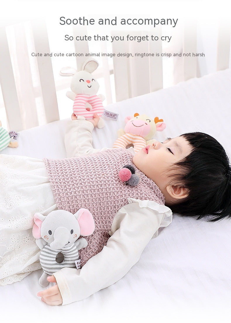 A baby lying on a white bed with various plush toys, including an elephant and a bunny, near them. The infant wears a pink knitted vest over a white outfit.