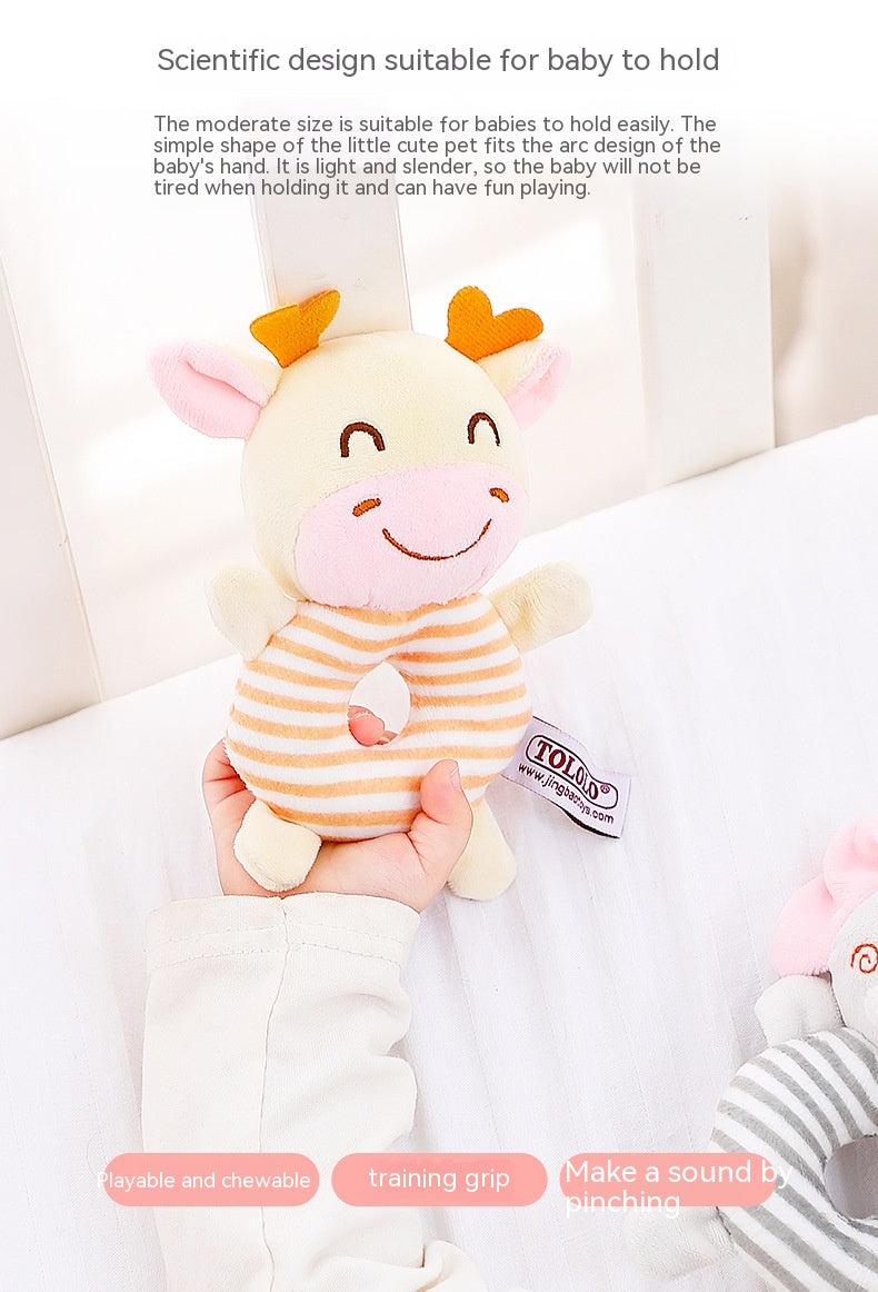 A baby's hand holds a cute cow plush toy with a striped, doughnut-shaped body. The toy has a friendly face with pink accents, making it easy and fun for babies to grip.