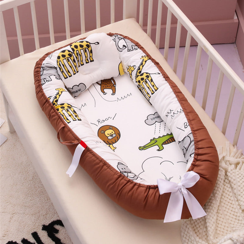 A baby nest with a brown border and animal print in a crib. It features giraffes, lions, and crocodiles with soft cushioning and a white bow on the edge.