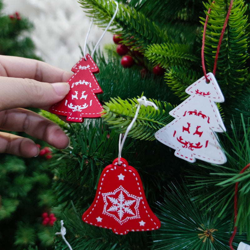 A hand decorating a Christmas tree with red and white ornaments shaped like trees and a bell, featuring festive designs.
