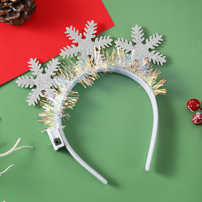 Festive headband with glittery silver snowflakes and sparkling tinsel sits on a green and red background. Accompanied by pine cone, small branch, and red berries.