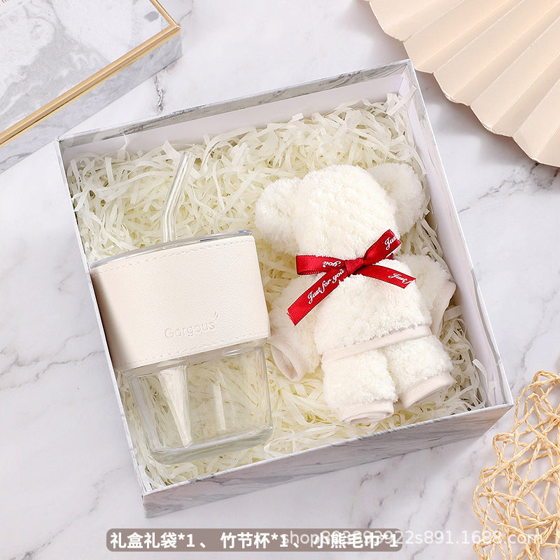 Gift box with a clear glass tumbler wrapped in a white holder and a fluffy white teddy bear adorned with a red ribbon. The box is filled with white shredded paper.