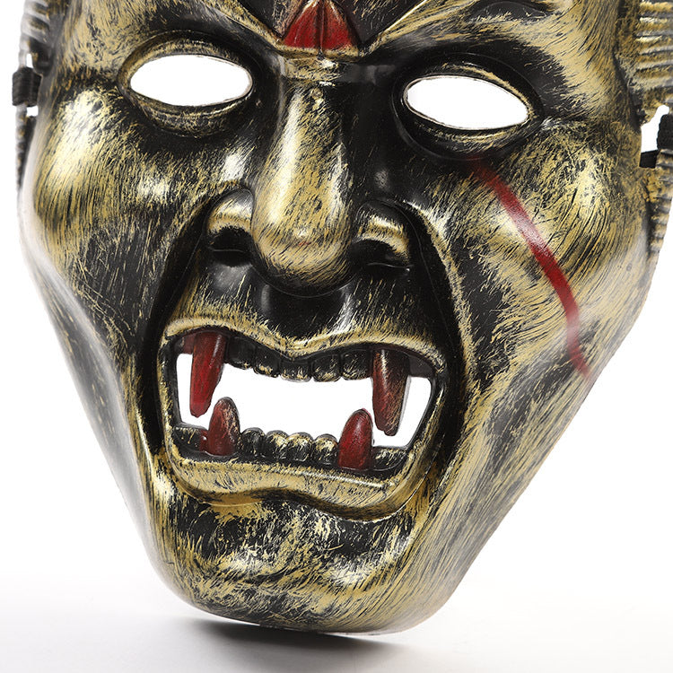 A fierce metallic mask with gold and black brushstrokes, featuring sharp red fangs, hollow eyes, and a prominent red scar on the right cheek, resembling a demonic face.
