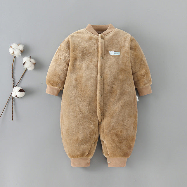 A soft, brown, fleece baby romper with snap buttons and a small patch on the chest is displayed on a gray background. Two cotton sprigs lie to the left of the romper.