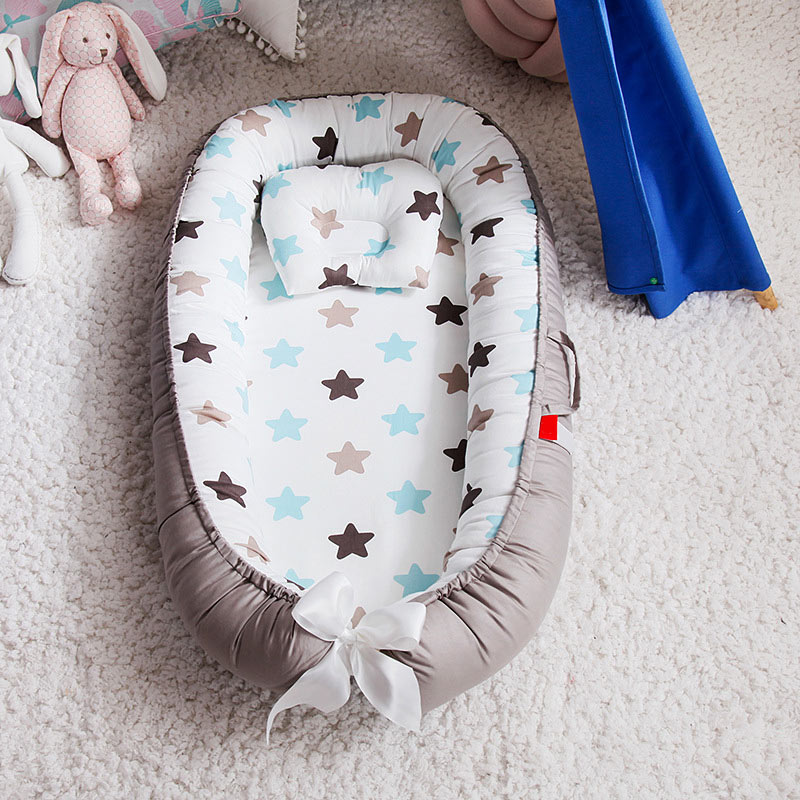 Cozy baby nest with soft gray sides and a star-patterned interior featuring blue, brown, and beige stars. It's placed on a fluffy white carpet, surrounded by plush toys.
