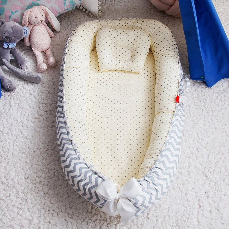 Cozy baby bed with polka dot lining and chevron-patterned edges, adorned with a white bow. Plush toys, including a pink rabbit and gray elephant, are nearby on a soft carpet.