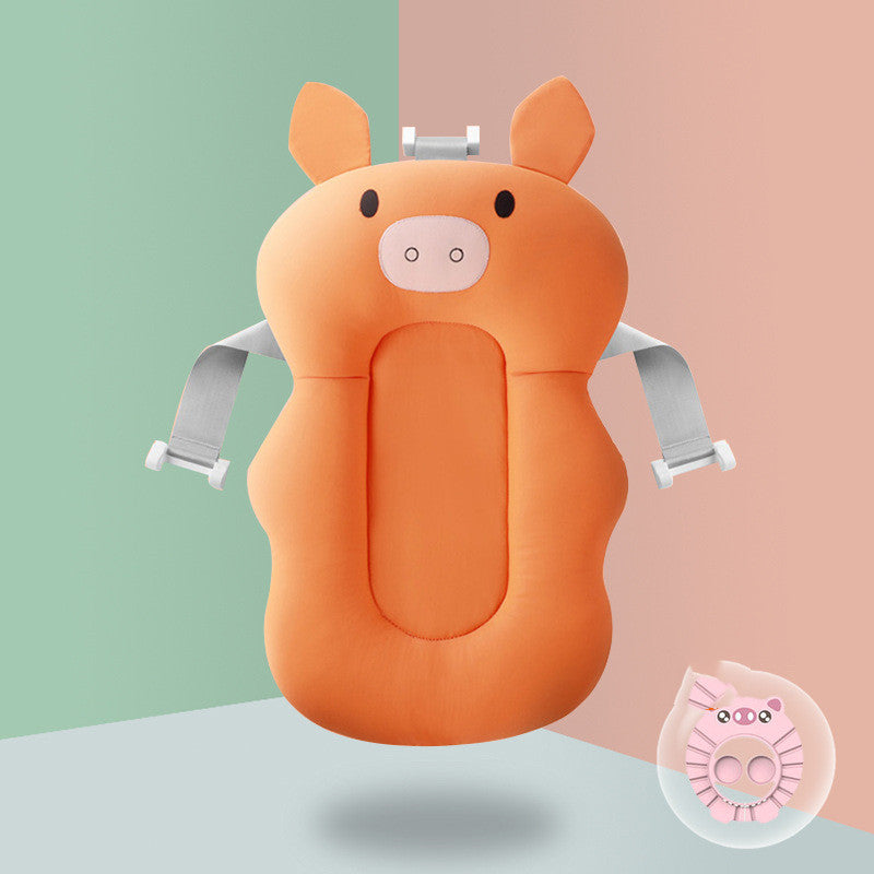 Orange pig-shaped baby bath cushion with gray straps against a split green and pink background. An inset shows a pink version of the cushion.