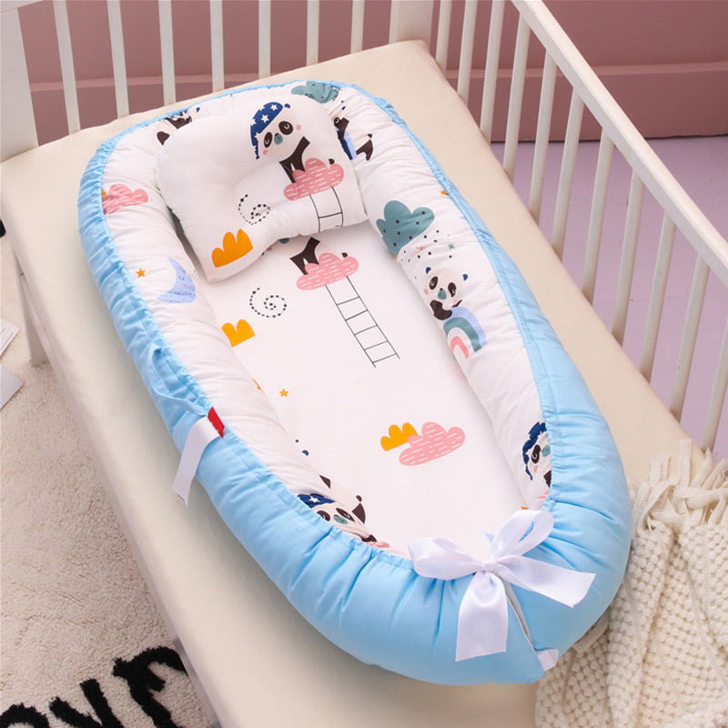 Baby cot with a colorful panda-themed cushion featuring clouds and rainbows, surrounded by a soft blue bumper, tied with a white ribbon, placed in a white crib.