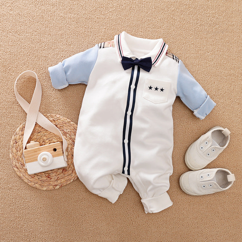 Baby outfit featuring a white onesie with blue sleeves, navy bow tie, and star detail, alongside small white shoes and a wooden toy camera on a woven mat.