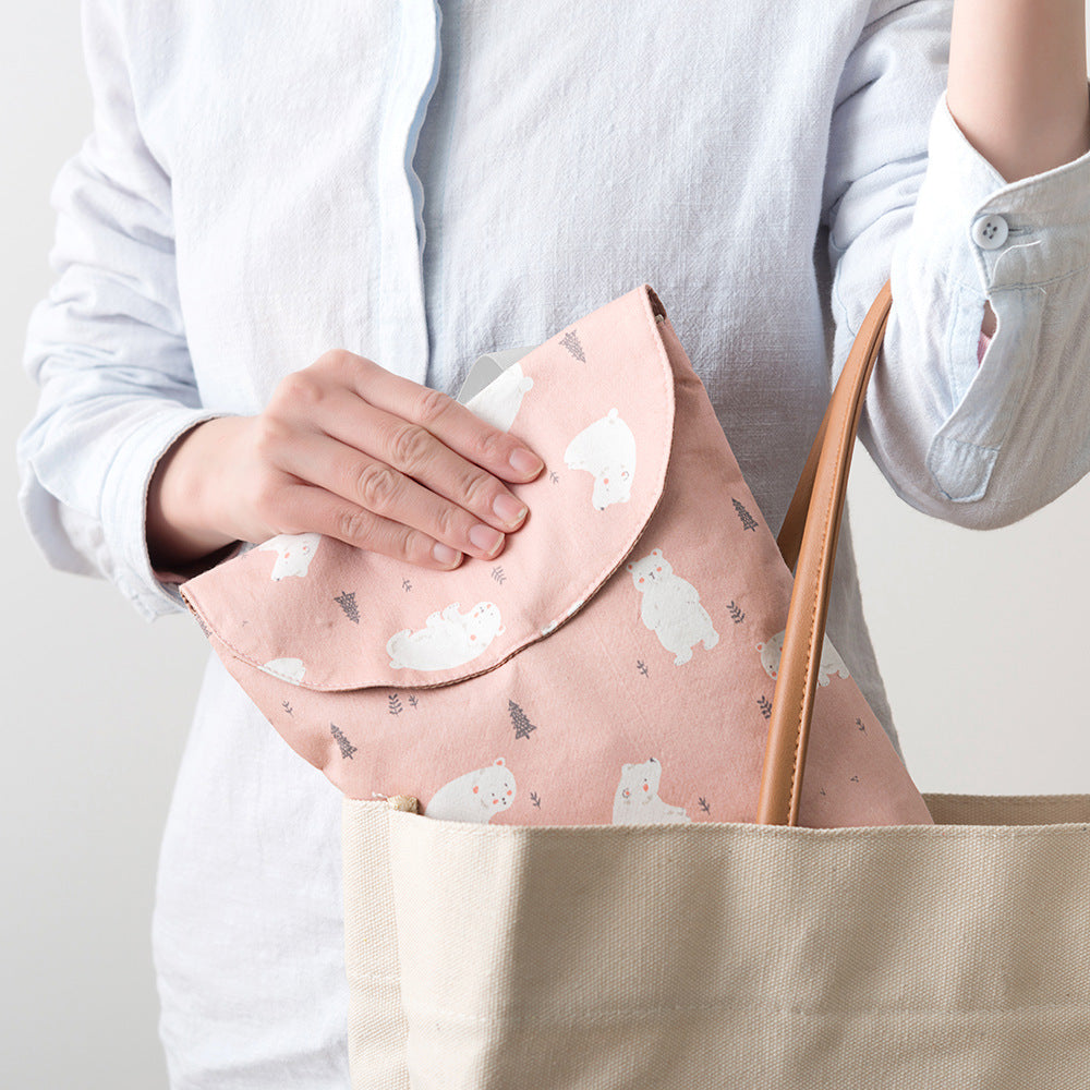 Person in a white shirt places a pink pouch with polar bear print into a beige tote bag with brown handles.