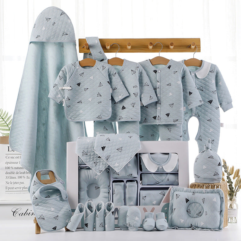 A set of baby clothes and accessories in light blue with paper airplane patterns, neatly arranged. Includes jackets, pants, bibs, a hat, shoes, and a large hooded towel.