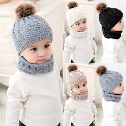 A young child wearing a white sweater models various knitted hats and scarves with pom-poms in gray, cream, black, and beige, displaying front and side views.