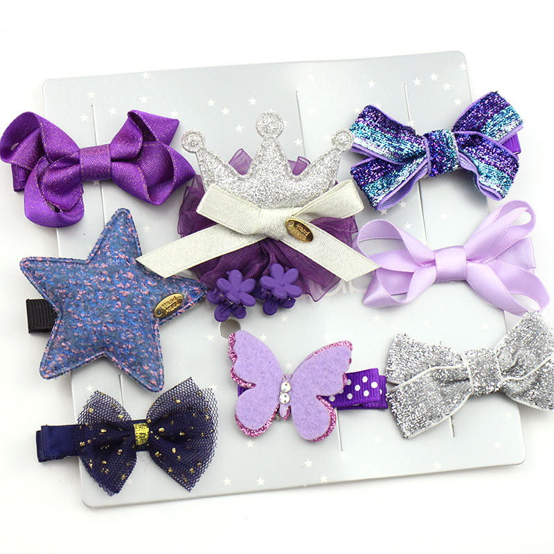 A collection of purple and silver hair accessories on a star-patterned card, including bows, a glittery crown, a butterfly, and a star-shaped clip.