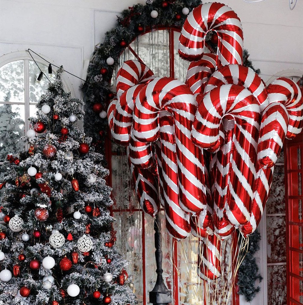 A festive scene with a snow-dusted Christmas tree adorned with red and white ornaments. Nearby, red and white striped candy cane balloons add a playful touch to the decor.