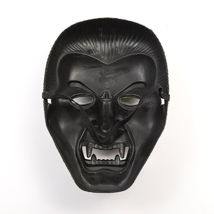 Black mask with an expression of open mouth and bared fangs, resembling a menacing face. The surface is shiny, with two holes for eyes and strings attached for wearing.