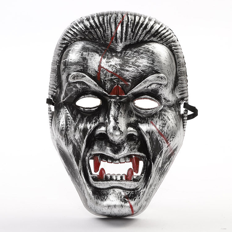A metallic vampire mask with red blood streaks and prominent fangs, featuring a menacing expression. The mask has cutouts for eyes and black straps on each side.