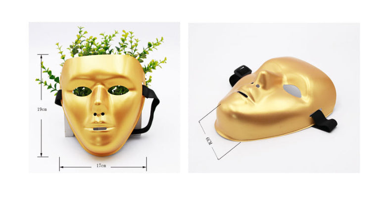 Gold face mask planter with green leaves emerging. Mask dimensions are 19cm by 17cm. Side view shows 6cm depth. Black straps are attached for mounting or wearing.