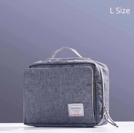A gray fabric travel toiletry bag with a handle and a front zipper pocket is shown against a gray background. It features a small label on the front and is labeled "L Size" in the corner.