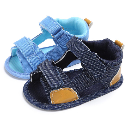 Two pairs of baby sandals; one in light blue fabric and the other in dark denim with tan accents. Both have adjustable straps and soft inner linings, designed for comfort.