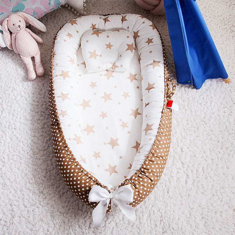 Cozy baby nest with a star-patterned interior and a polka dot brown border, featuring a white bow at the bottom. A pink plush toy and blue play tent are nearby on a soft carpet.