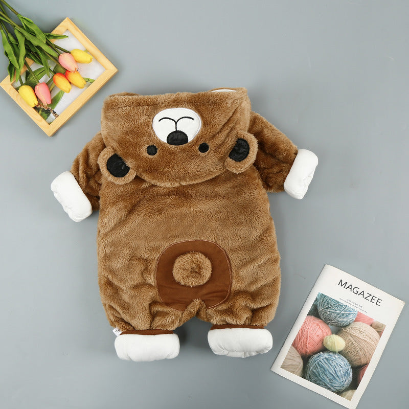 A fluffy brown bear-shaped baby onesie with white paws and ears is laid out on a gray surface. Nearby are a wooden frame with colorful tulips and a magazine featuring yarn balls.