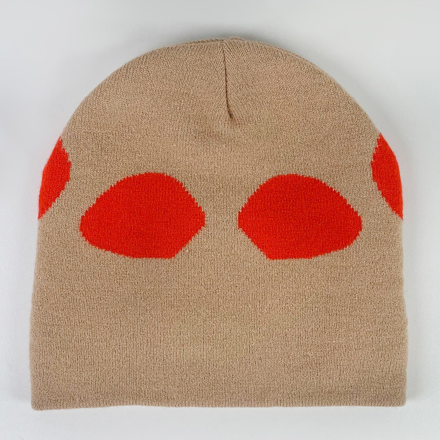 Beige knit beanie with four bold red half-circle shapes on the front, evenly spaced. Simple and modern design against a plain white background.
