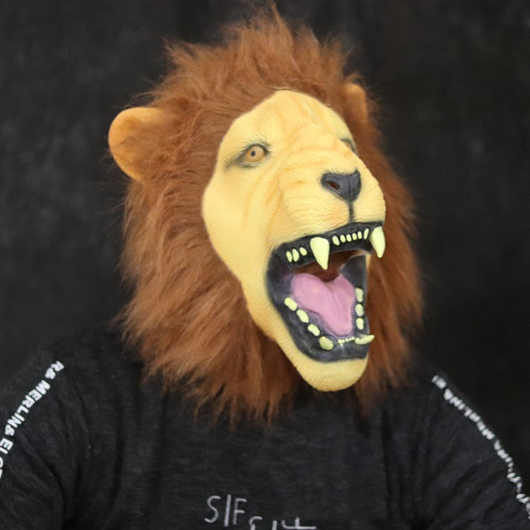 Person wearing a realistic lion mask with an open mouth, displaying sharp teeth. The mask has a detailed mane and the person is dressed in a black shirt with white text.