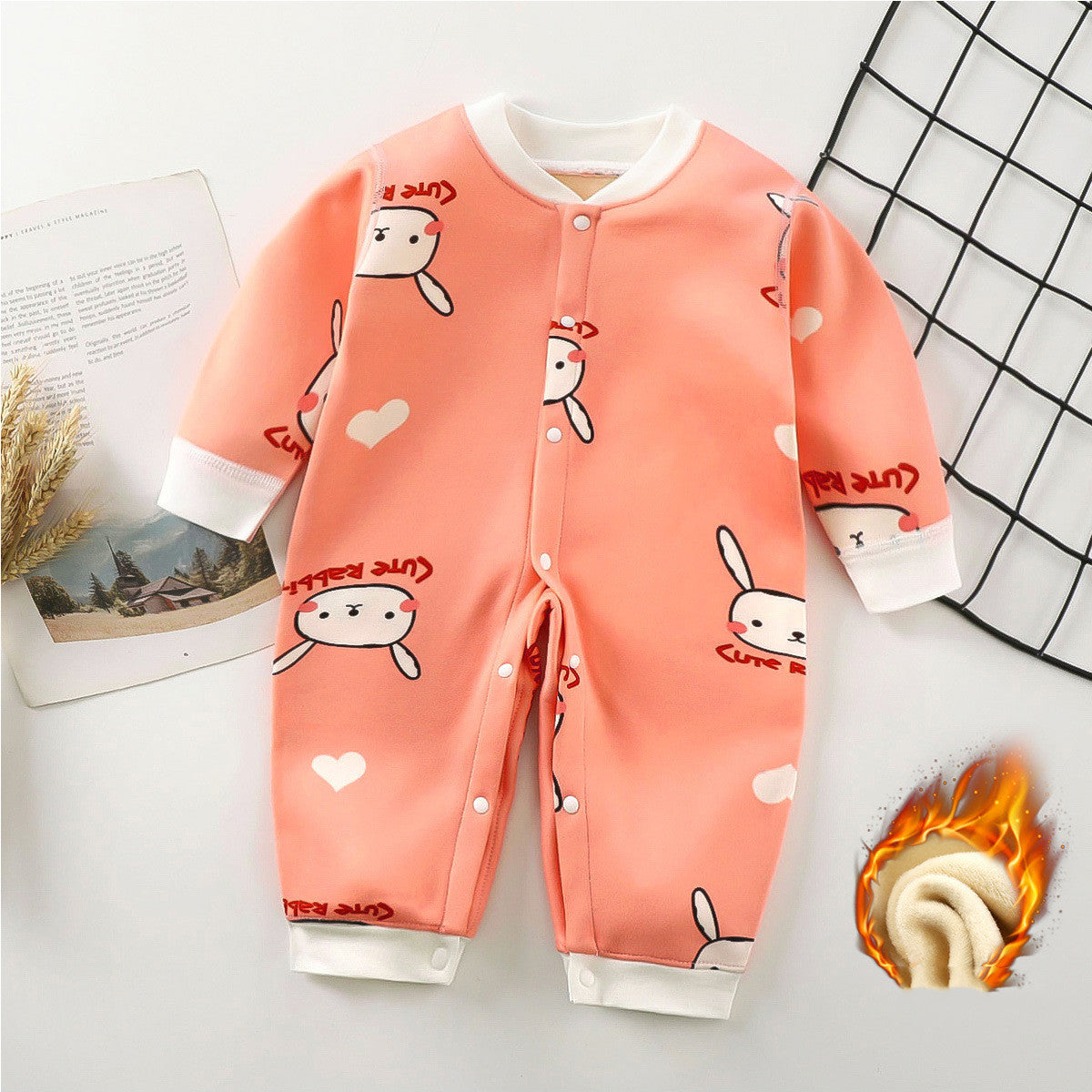 Peach-colored baby romper with cartoon rabbits, hearts, and "Cute Rabbit" text. White cuffs and snap buttons. Grid and magazine background with a fabric texture detail shown.