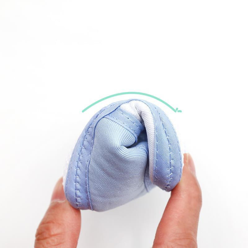 A hand squeezing a soft, blue fabric object, demonstrating its flexibility. A green curved arrow above indicates the bending motion. The background is plain white.