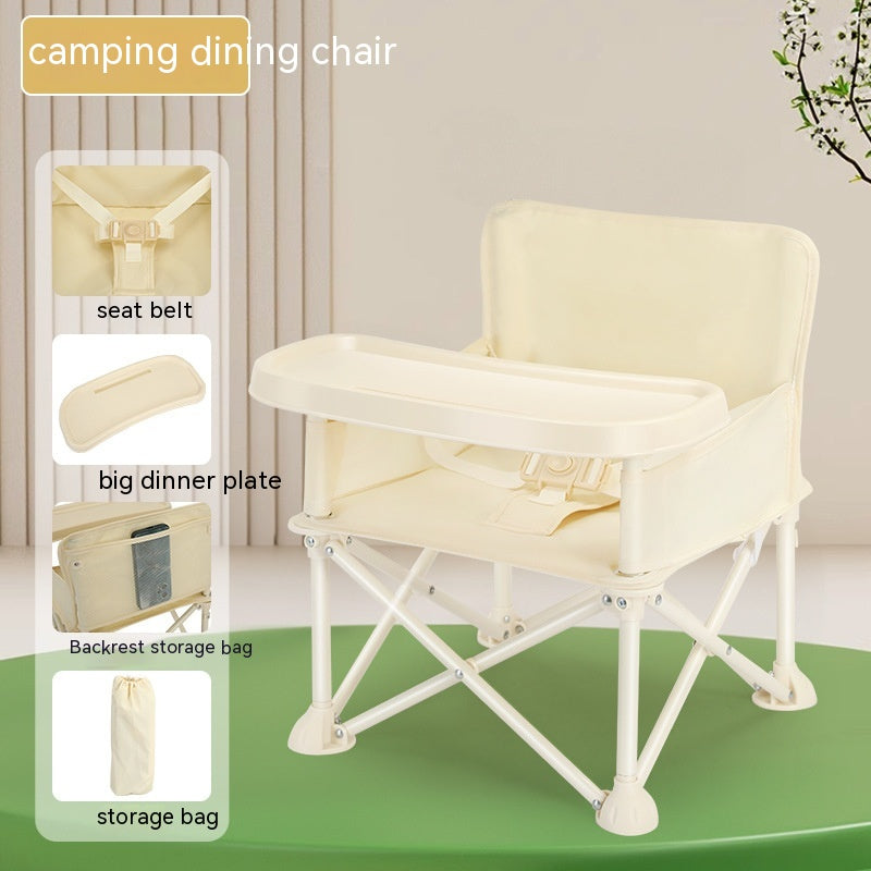 Cream camping dining chair with a seat belt, large dinner tray, and backrest storage bag. Comes with a storage bag. Placed on a green platform against a curtain backdrop.