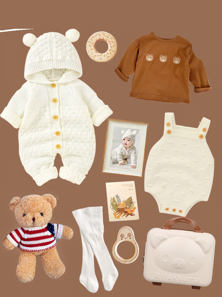 Baby outfit set on brown background includes a white bear-ear hooded romper, bear-themed brown top, cream romper, teddy bear, socks, wooden toys, a framed photo, and a Rilakkuma suitcase.