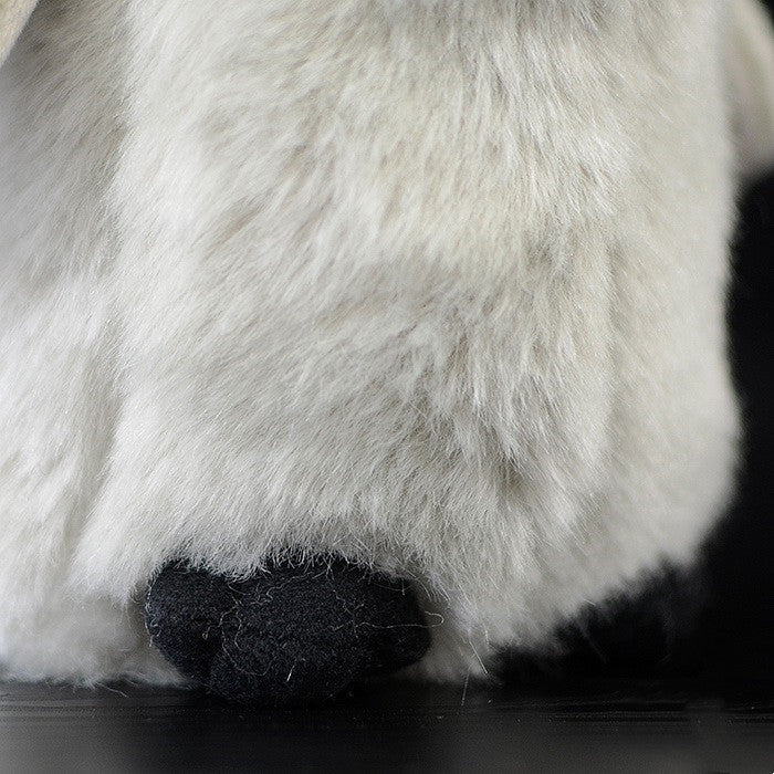 Close-up of a plush toy's paw, featuring soft white fur and a small black felt pad at the bottom, set against a dark background.