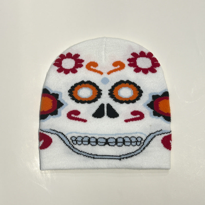 White beanie featuring a colorful Day of the Dead sugar skull design with orange, black, and red floral patterns, circles around the eyes, and a wide toothy smile.