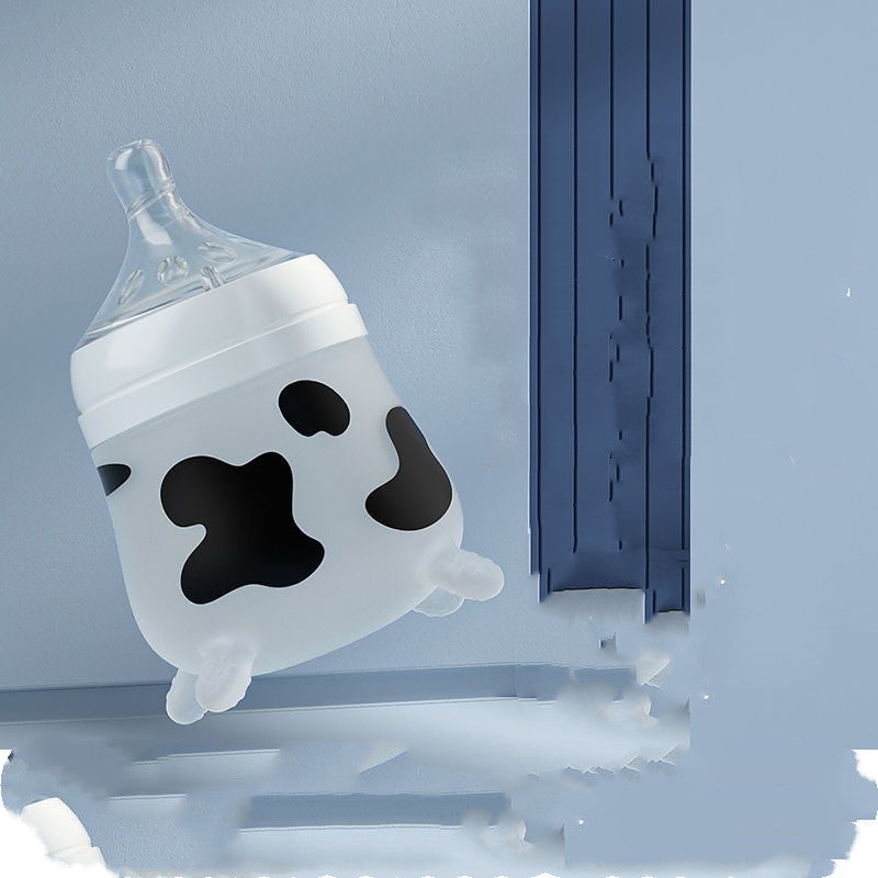 A baby bottle with a cow pattern, featuring black spots on a white background, rests on a light blue surface near a similarly colored wall and trim.