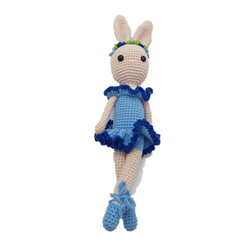 Crocheted bunny wearing a blue dress with dark blue ruffles and matching shoes. It has a flower headband and is set against a plain white background.