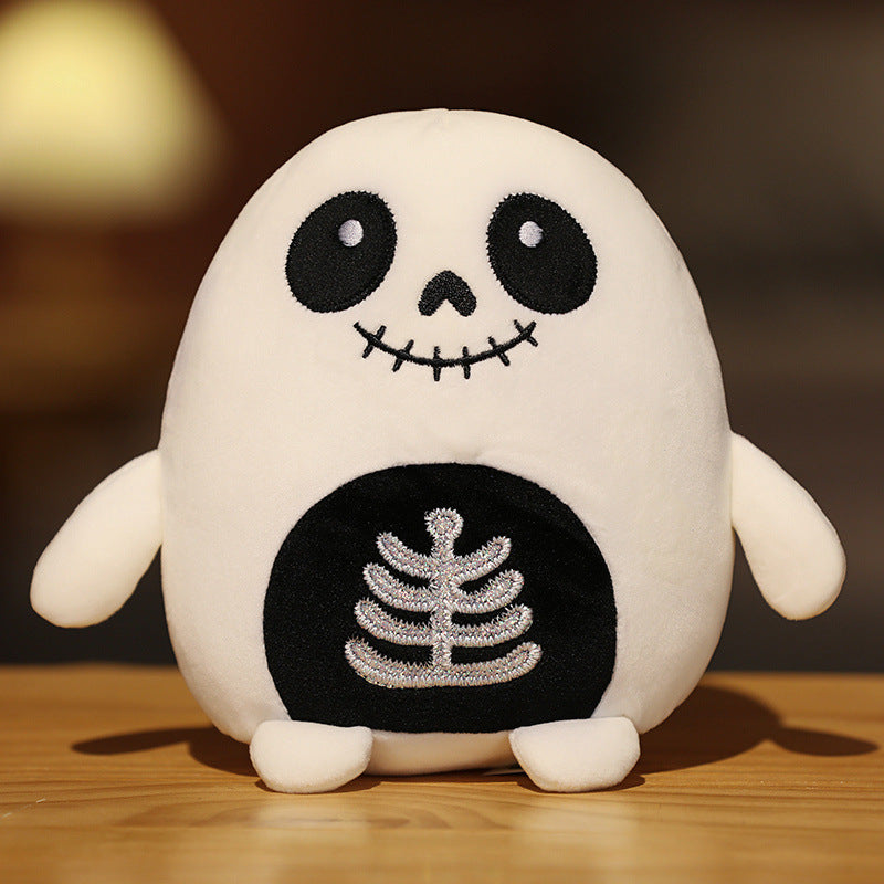 Cute plush toy with a skeleton design, featuring a round body, large black eyes, and stitched mouth. It has a ribcage pattern on its belly and is set on a wooden surface.