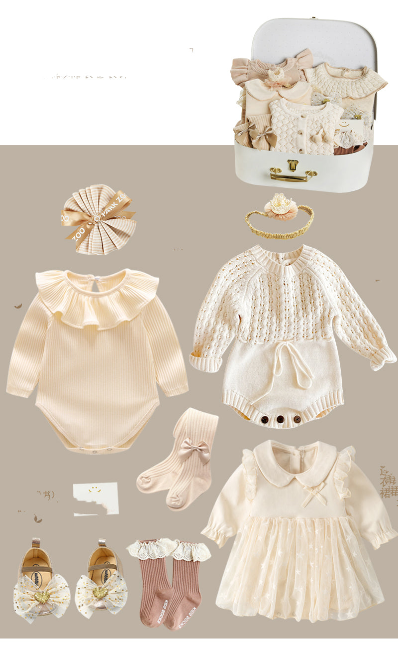 Baby clothing set with cream and beige tones includes onesies, dresses, socks, and a headband. Accessories are elegantly arranged alongside a small suitcase.