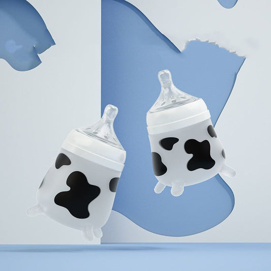Two baby bottles with cow patterns float in front of a blue and white abstract background, featuring clear nipples and black spots, blending playful and functional design.