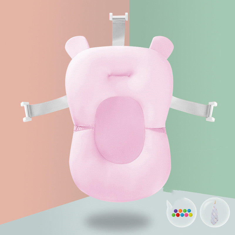 Pink baby bath cushion with white adjustable straps and bear ears on a soft pastel background. Two icons showing colorful balls and an arrow are at the bottom right.