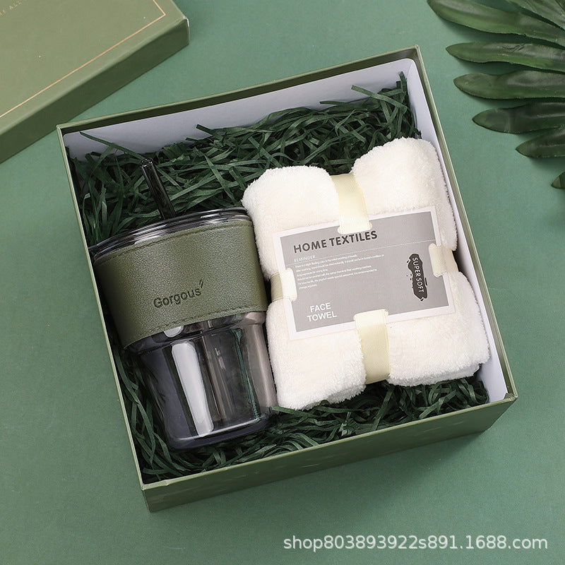 Gift box with a green travel tumbler labeled "Gorgous" and a white face towel labeled "Home Textiles." The box is lined with green shredded paper.