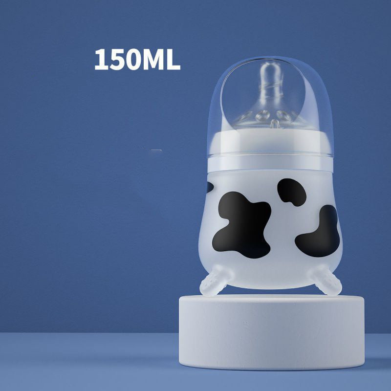 Baby bottle with a cow print design, 150ml capacity, and a silicone nipple, placed on a round white pedestal against a blue background.