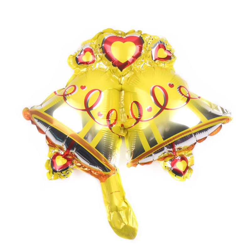Two yellow foil balloons shaped like bells with red heart motifs and swirl designs, connected at the top. The reflective surface suggests a festive or celebratory theme.