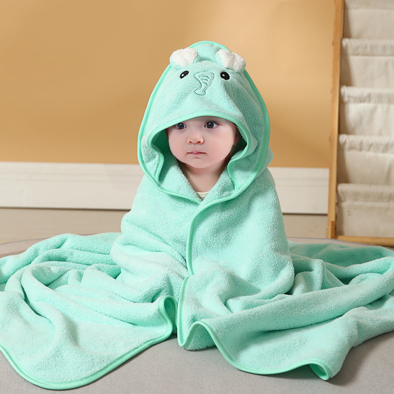 A baby is wrapped in a soft, mint green hooded towel with bear ears, sitting on a carpeted floor against a beige wall. The baby looks calm and relaxed.