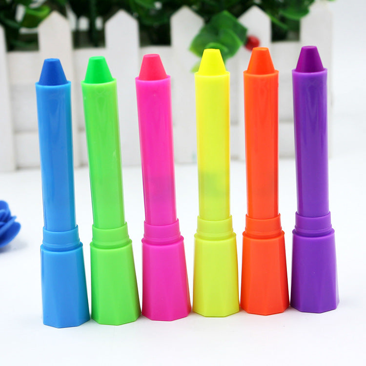 Six vibrant marker pens stand upright in a row, featuring blue, green, pink, yellow, orange, and purple colors. A white fence and greenery are blurred in the background.