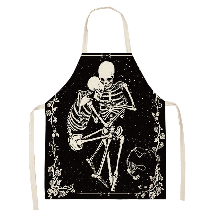 Apron with a gothic design featuring two embracing skeletons surrounded by floral and vine decorations on a black background. White ties and neck strap contrast with the dark fabric.