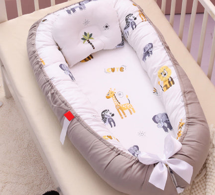 A cozy baby crib nest with a beige border, featuring a white mattress adorned with cute animal prints, including giraffes, lions, and elephants. A matching pillow is included.