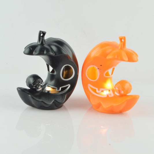 Two crescent-shaped pumpkin candle holders, one black and one orange, each with a grinning face and a small skull. Both contain lit candles, casting a warm glow.